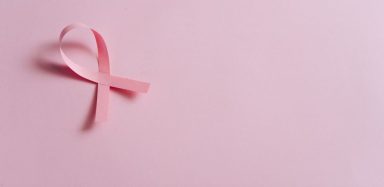 A breast cancer ribbon on a light pink background.