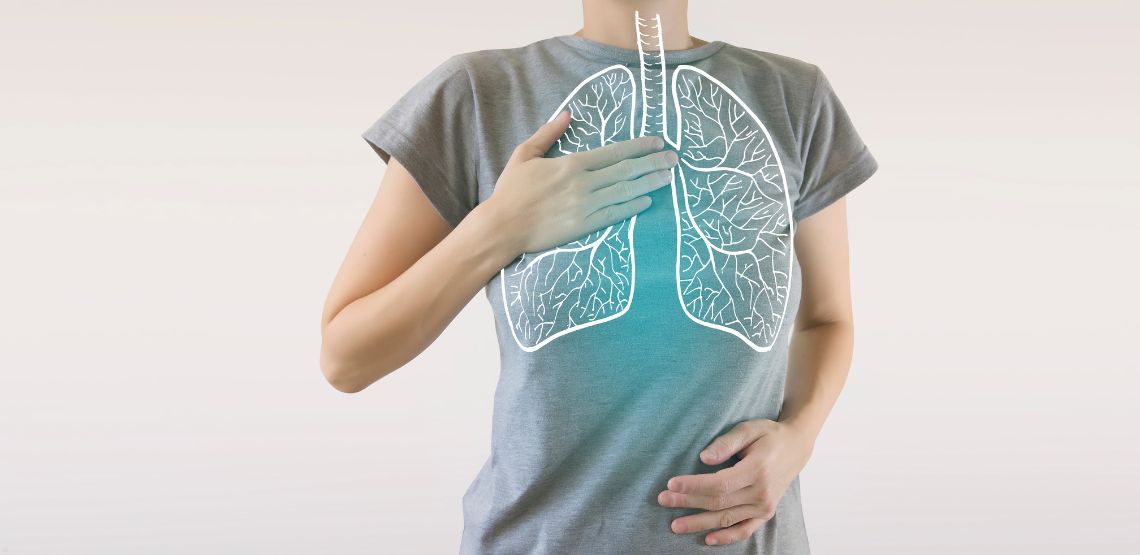 An image of a woman in a grey t-shirt with a hand on her chest. There is a digital drawing of white lungs over her chest.