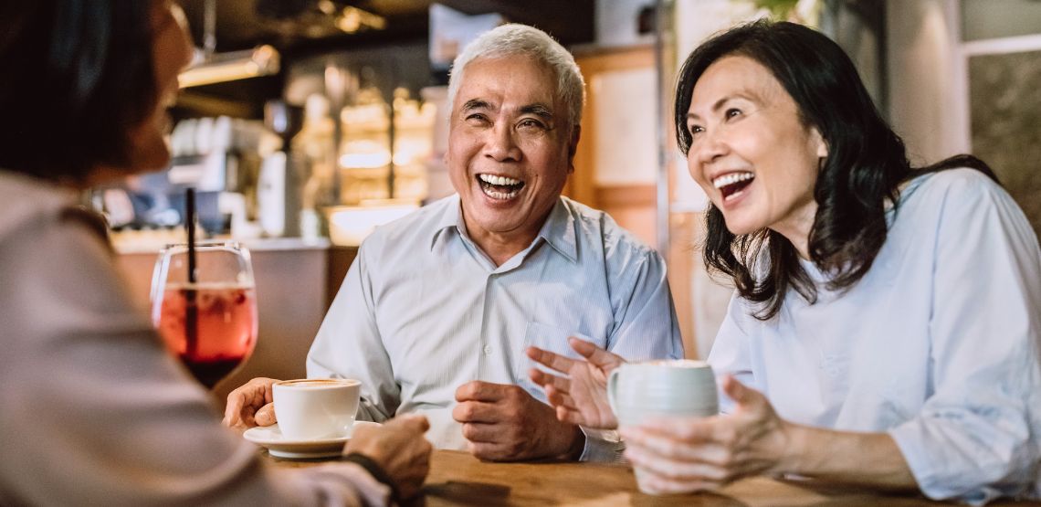 An older couple smiling while having coffee with friends.